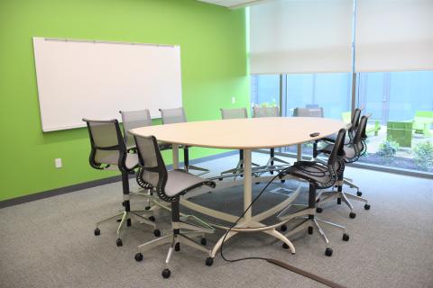 A high-top table with ten chairs and a large mounted whiteboard. 