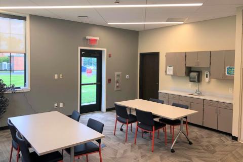 Two tables with four chairs at each table. Cabinets with a sink on the right wall.