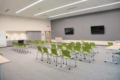 37 chairs facing the front of the room. Two large mounted televisions. Cabinets and sink on the left wall. Five tables available to be placed. 