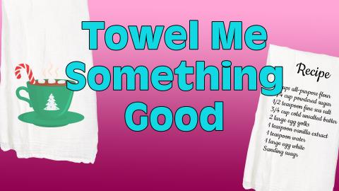 Image reads "Towel Me Something Good" against a pink gradient background, A tea towel with a cup of cocoa is to the left of the title. A tea towel with a recipe on it is to the right of the title.