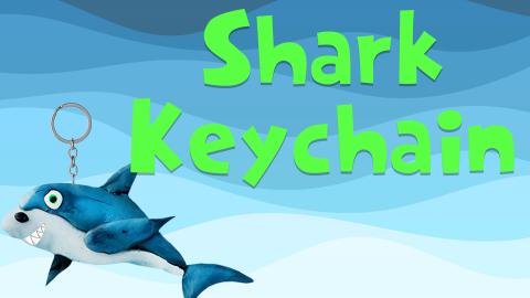 Image reads "Shark Keychain" against a blue wavy background. A clay shark keychain is to the left of the title.