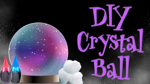 Image reads "DIY Crystal Ball" against a black misty background. A crystal ball is to the left of the title with 2 things of food coloring and cotton balls.