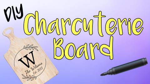 Image reads "DIY Charcuterie Board" against a gradient background. A decorated charcuterie board is to the left of the title. A paint marker is to the right of the title.