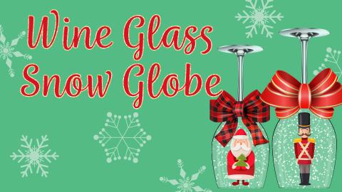 Image reads "Wine Glass Snow Globe" against a green background. Two wine glasses turned upside are to the right of the title. Each glass is filled with snow and has a Christmas figurine inside the glass. 