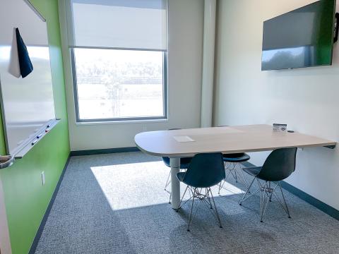 A table attached to the wall with four chairs with a mounted television and a mounted white board.