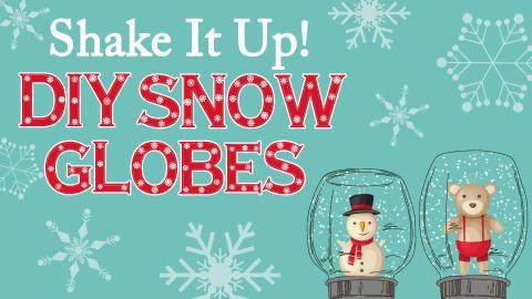 Image reads "Shake It Up! DIY Snow Globes" against a muted blue background. To the bottom right of the title are two snow globes with a snowman and a bear inside of them. There are snowflakes scattered among the image.