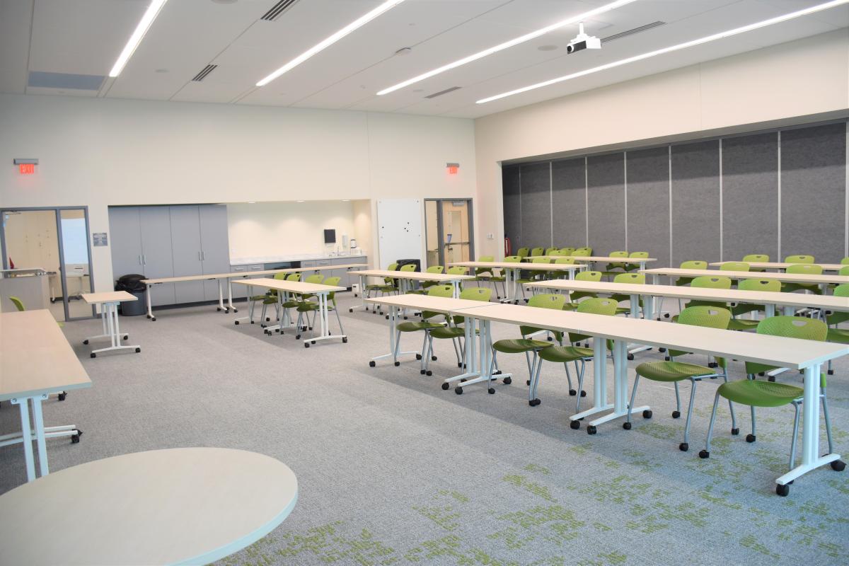 25 tables and 45 chairs set up to face the front. Shows cabinets and a sink on the left wall and a large mounted whiteboard.